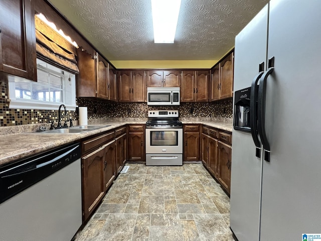 kitchen with appliances with stainless steel finishes, a sink, stone finish flooring, dark brown cabinets, and backsplash