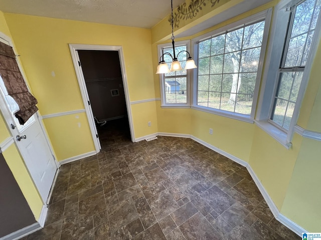 unfurnished dining area featuring a notable chandelier, stone finish flooring, a textured ceiling, and baseboards