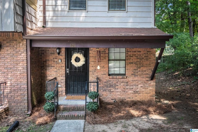 doorway to property with brick siding and roof with shingles