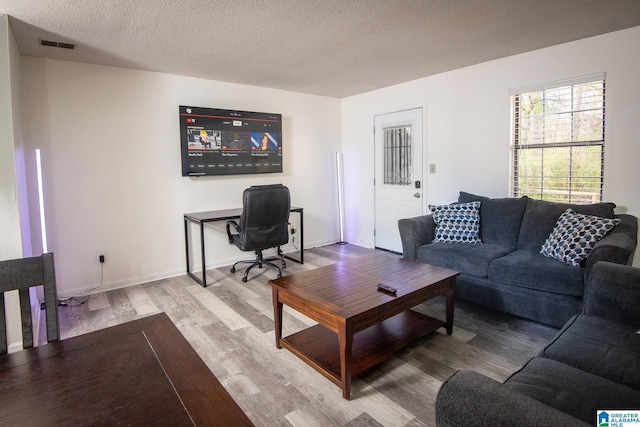 living area featuring a textured ceiling, wood finished floors, visible vents, and baseboards