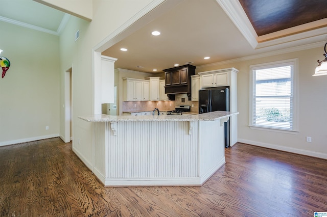 kitchen with gas range, dark wood-type flooring, a peninsula, light stone countertops, and crown molding