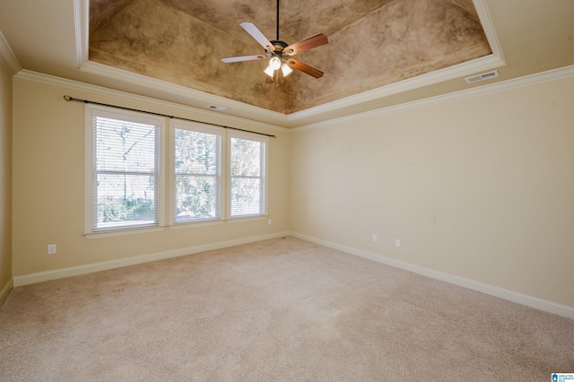 carpeted empty room with ornamental molding, a raised ceiling, visible vents, and baseboards