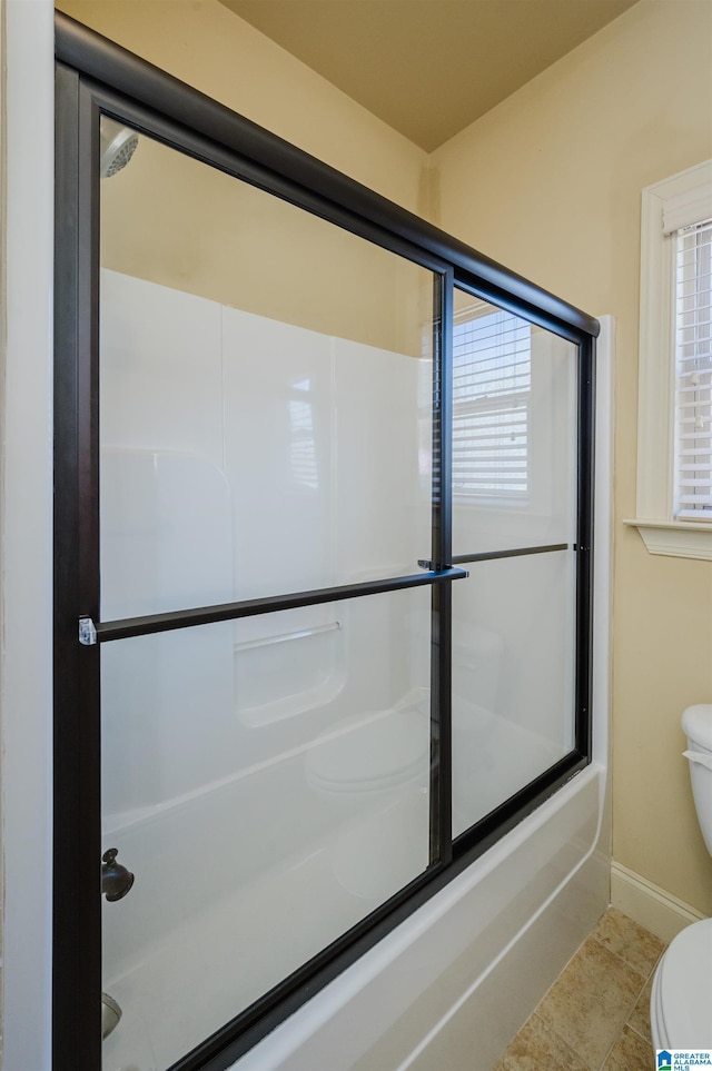 bathroom featuring tile patterned flooring, baseboards, toilet, and bath / shower combo with glass door