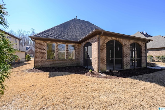 rear view of house featuring brick siding, roof with shingles, fence, and a sunroom