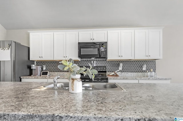 kitchen with freestanding refrigerator, black microwave, white cabinets, and decorative backsplash