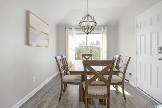 dining space with a notable chandelier, vaulted ceiling, wood finished floors, and baseboards