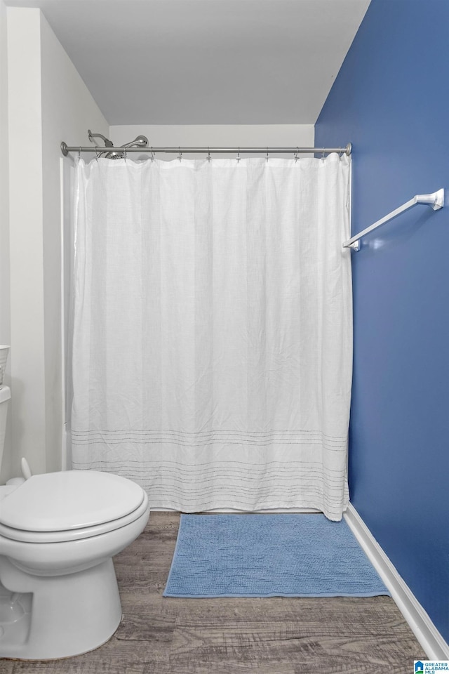 bathroom featuring baseboards, wood finished floors, toilet, and a shower with curtain