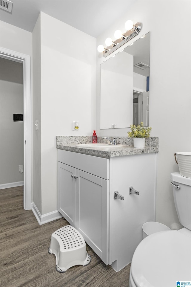 half bath with visible vents, vanity, toilet, and wood finished floors