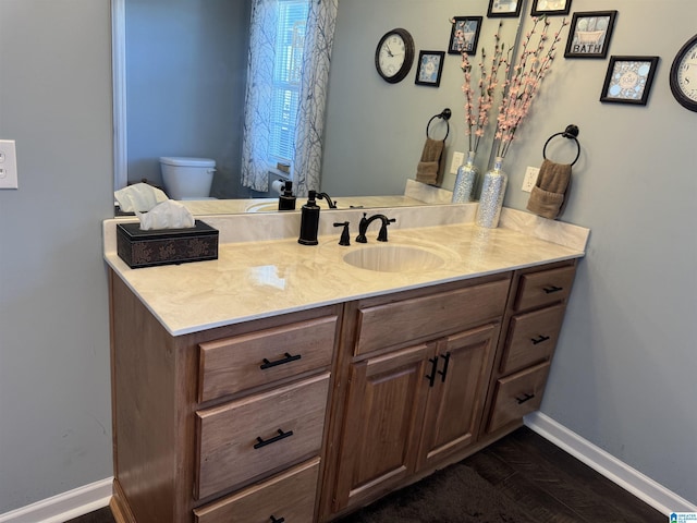 bathroom with toilet, vanity, baseboards, and wood finished floors