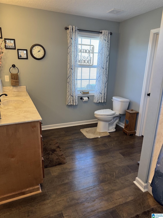 bathroom with a textured ceiling, wood finished floors, toilet, and baseboards