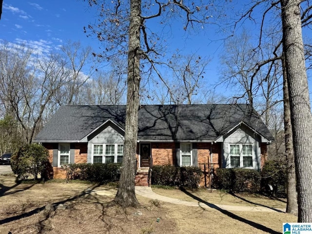 view of front of home featuring roof with shingles, dirt driveway, and brick siding