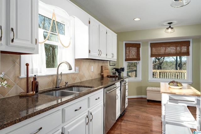 kitchen featuring baseboards, dark stone counters, white cabinets, dishwasher, and a sink