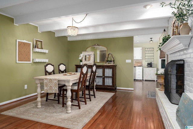 dining room featuring a chandelier, baseboards, a brick fireplace, beamed ceiling, and dark wood finished floors