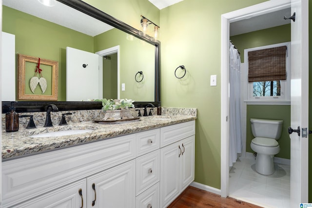 bathroom featuring baseboards, a sink, toilet, and double vanity