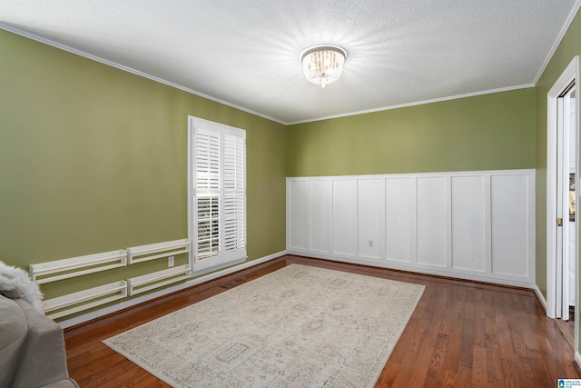 empty room featuring wainscoting, crown molding, a textured ceiling, and wood finished floors