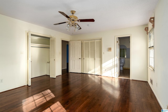 unfurnished bedroom with a ceiling fan, visible vents, dark wood finished floors, ensuite bath, and two closets