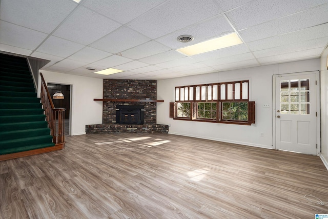 unfurnished living room with visible vents, baseboards, a drop ceiling, stairs, and wood finished floors