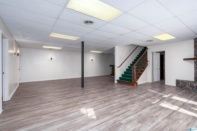 finished below grade area featuring visible vents, baseboards, a drop ceiling, stairs, and wood finished floors