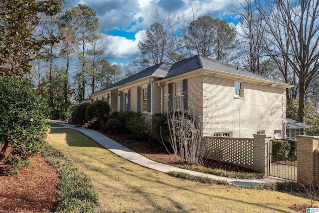 view of side of home with a gate, brick siding, and a yard