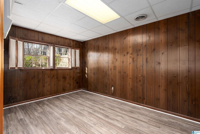 spare room featuring wooden walls, visible vents, baseboards, light wood-style flooring, and a paneled ceiling