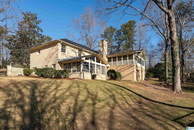 rear view of house with a lawn, a chimney, and a sunroom