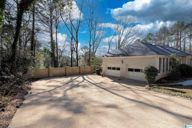 view of side of property featuring an attached garage, fence, brick siding, and driveway