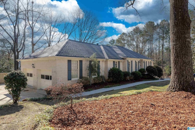 view of side of property with brick siding, an attached garage, driveway, and roof with shingles