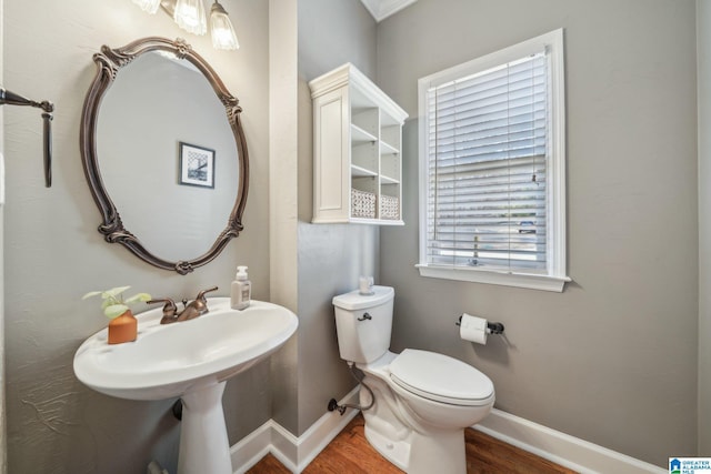 half bath with toilet, baseboards, and wood finished floors