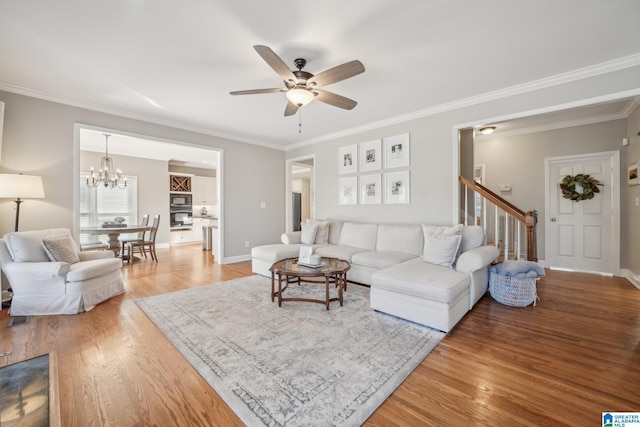 living room with crown molding, light wood finished floors, ceiling fan with notable chandelier, baseboards, and stairs