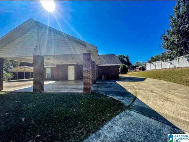 view of side of home featuring a patio, fence, a lawn, and brick siding