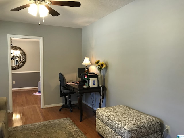 office with ceiling fan with notable chandelier, wood finished floors, and baseboards