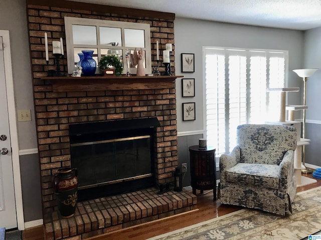 living area with a healthy amount of sunlight, a brick fireplace, baseboards, and wood finished floors