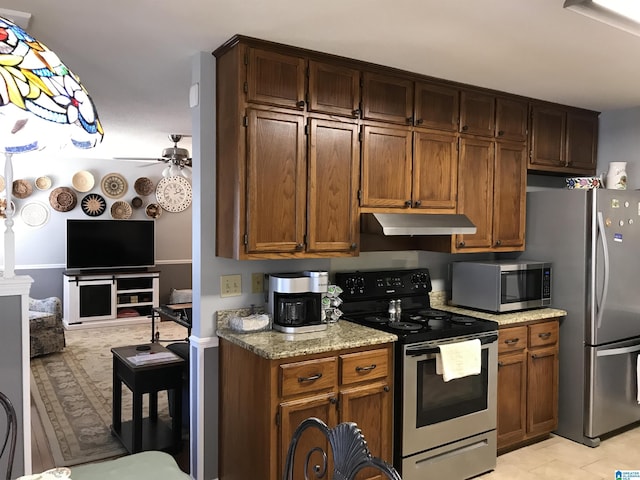 kitchen featuring light stone counters, a ceiling fan, under cabinet range hood, appliances with stainless steel finishes, and open floor plan