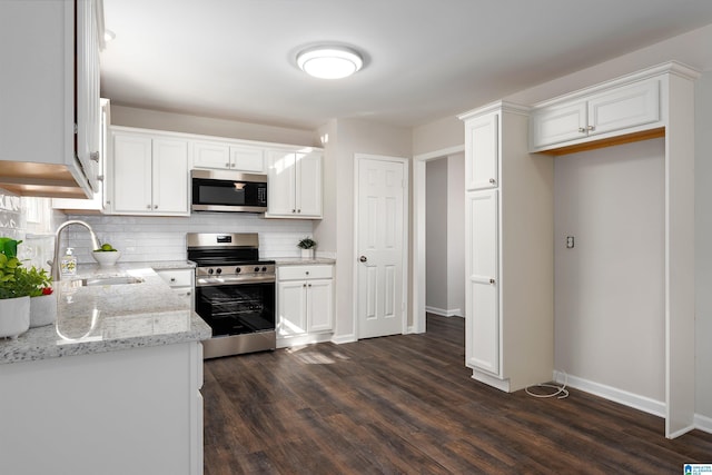 kitchen with white cabinets, dark wood finished floors, decorative backsplash, stainless steel appliances, and a sink