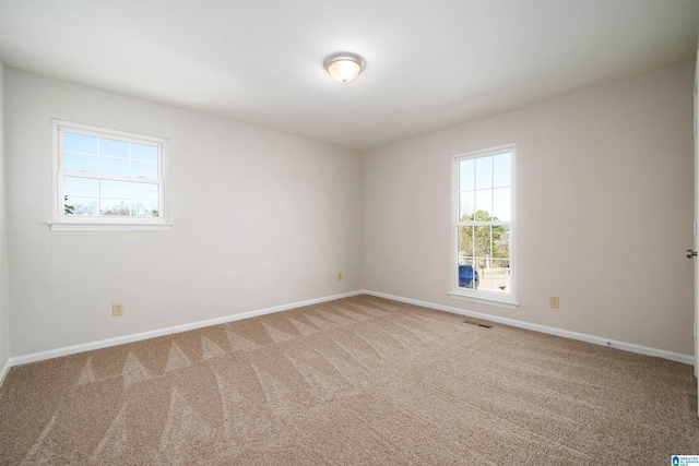 carpeted spare room featuring visible vents, baseboards, and a wealth of natural light