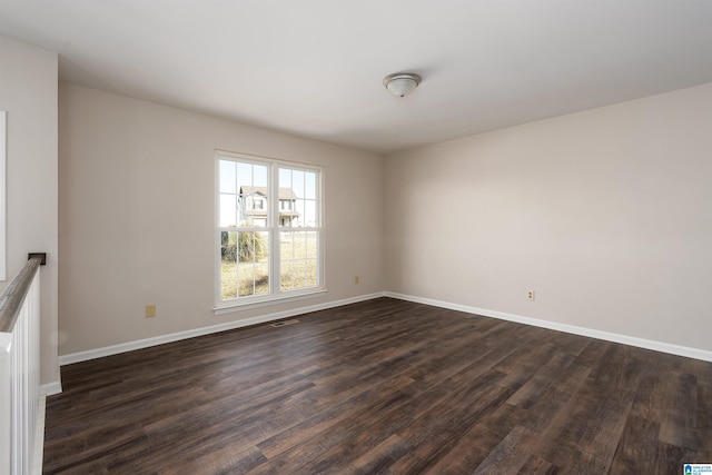 empty room with dark wood-style flooring, visible vents, and baseboards