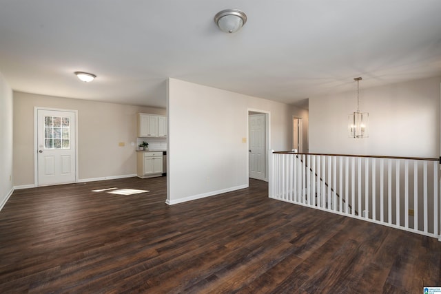 unfurnished room with a chandelier, dark wood finished floors, and baseboards