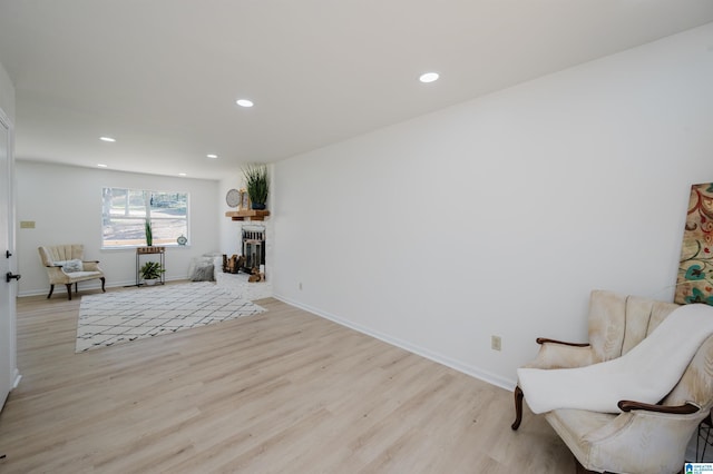 sitting room featuring light wood finished floors, recessed lighting, baseboards, and a glass covered fireplace