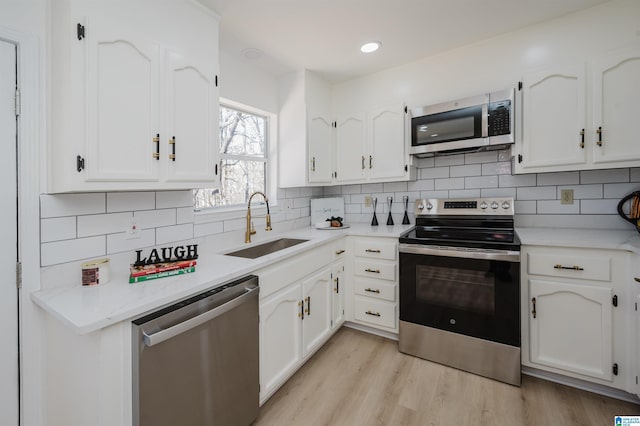 kitchen featuring tasteful backsplash, appliances with stainless steel finishes, light wood-style floors, white cabinetry, and a sink