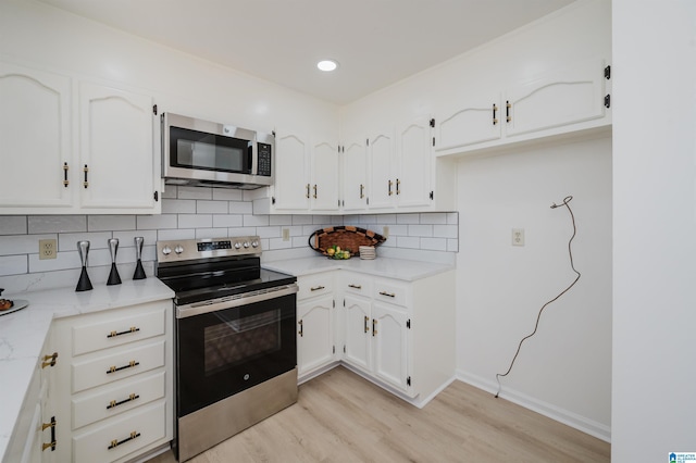 kitchen featuring appliances with stainless steel finishes, white cabinets, light wood finished floors, and decorative backsplash