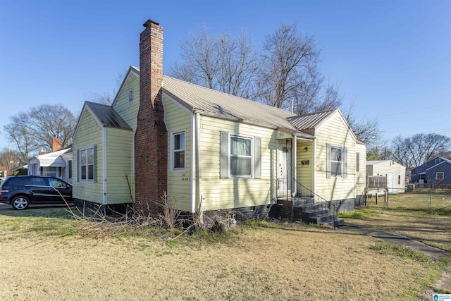 view of front facade with a front yard, metal roof, fence, and a chimney