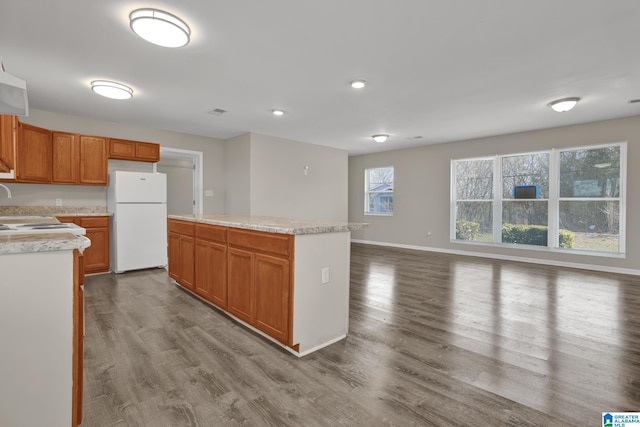 kitchen featuring baseboards, wood finished floors, a center island, freestanding refrigerator, and light countertops