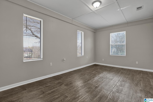 empty room with a wealth of natural light, dark wood-style flooring, visible vents, and baseboards