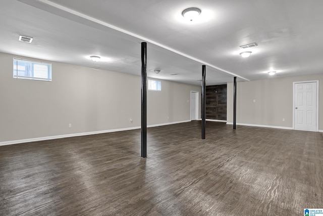 basement featuring visible vents, baseboards, and dark wood-style flooring