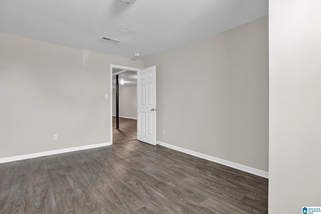 spare room with dark wood-style flooring, visible vents, and baseboards