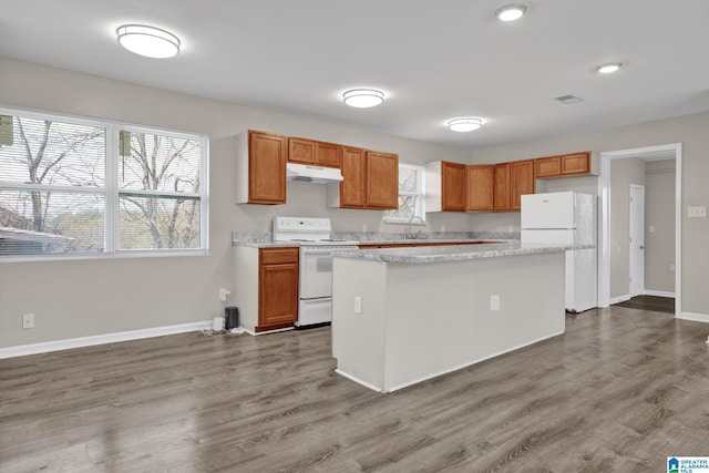 kitchen with under cabinet range hood, white appliances, dark wood-type flooring, a sink, and a center island