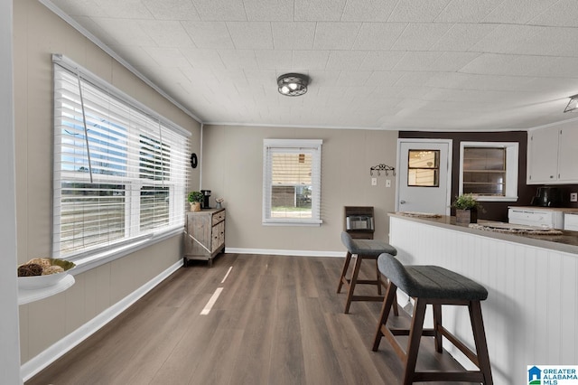 kitchen with heating unit, dark wood-type flooring, ornamental molding, white cabinetry, and a kitchen breakfast bar