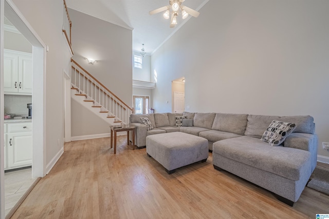 living area featuring light wood-style floors, a ceiling fan, high vaulted ceiling, baseboards, and stairs