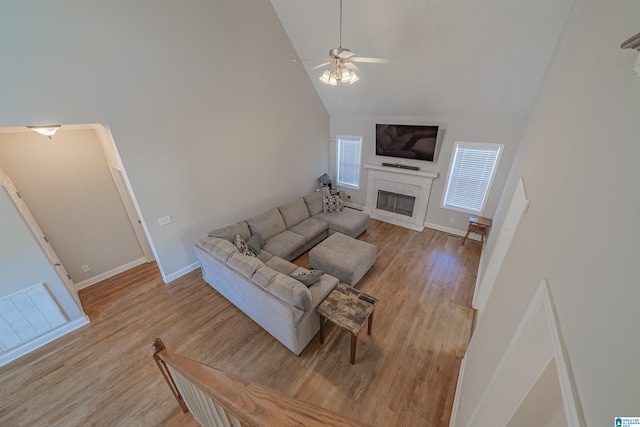 living area with light wood-style flooring, a ceiling fan, a glass covered fireplace, high vaulted ceiling, and baseboards