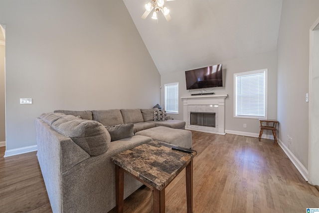 living room featuring high vaulted ceiling, a high end fireplace, baseboards, and wood finished floors